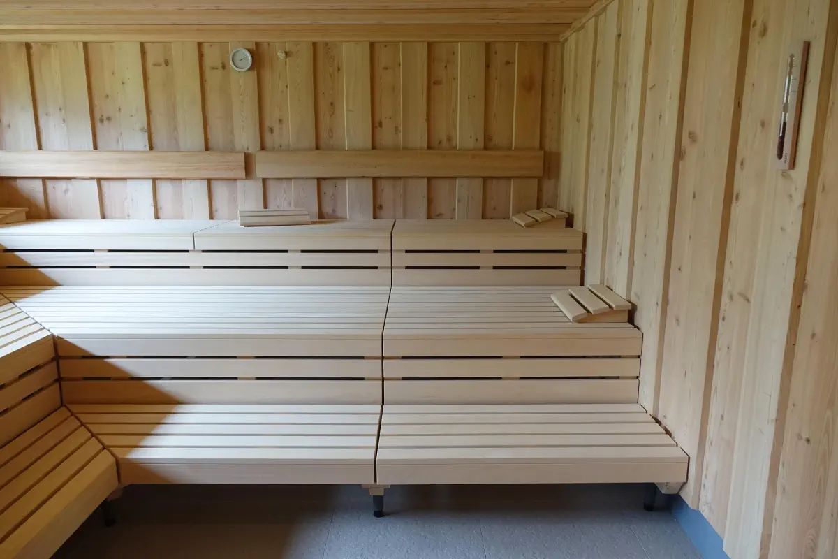 Warm wooden sauna with soft lighting, steam rising from rocks, and simple wooden bench