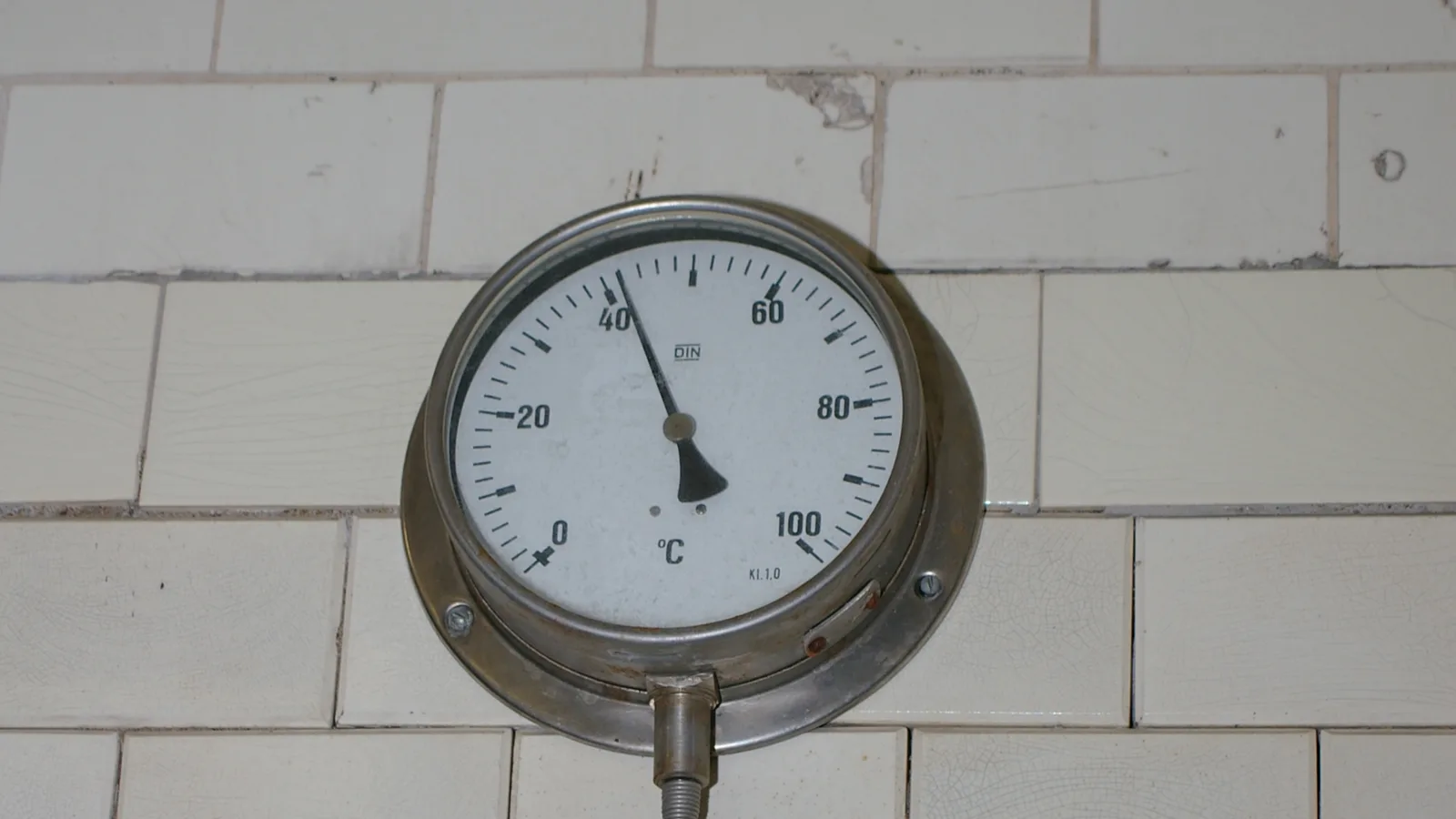 An old dial thermometer in degrees Celsius on the tiled wall of a historic sauna