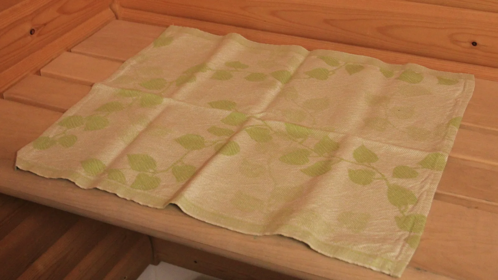 A linen sauna seat towel with a birch-leaf pattern laid on a wooden sauna bench
