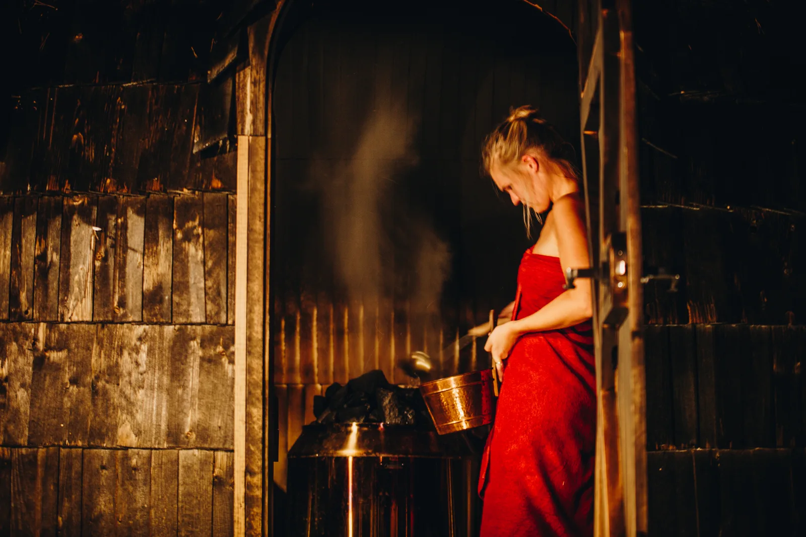 A bather ladling water onto the sauna stones, sending up a cloud of steam