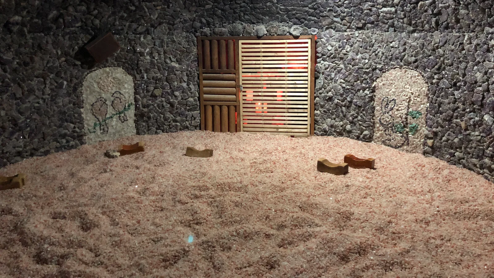 A heated jjimjilbang room in Korea with stone walls, a salt-covered floor and wooden block pillows