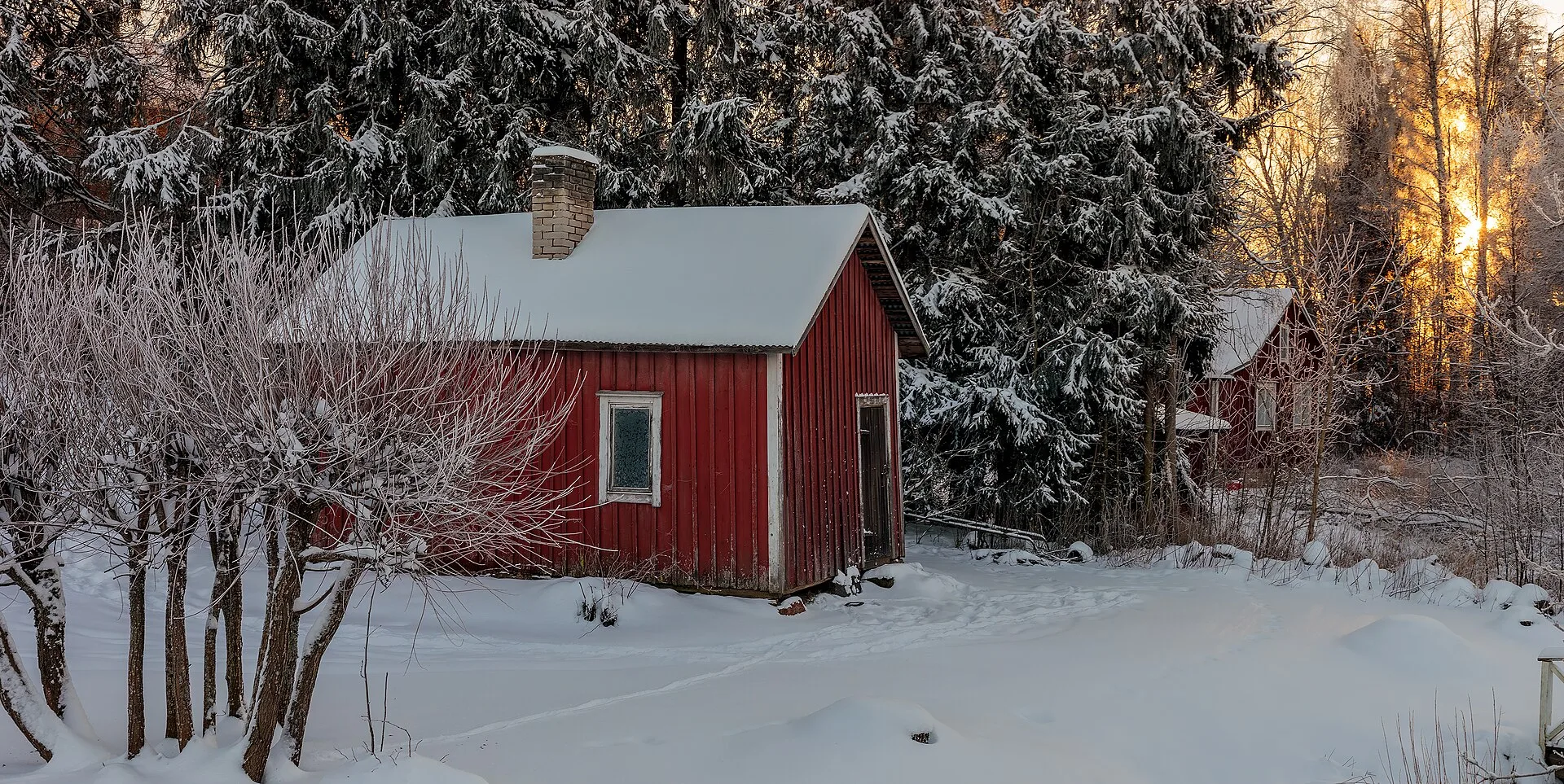 A red wooden sauna cabin in deep snow, lit by low winter sun